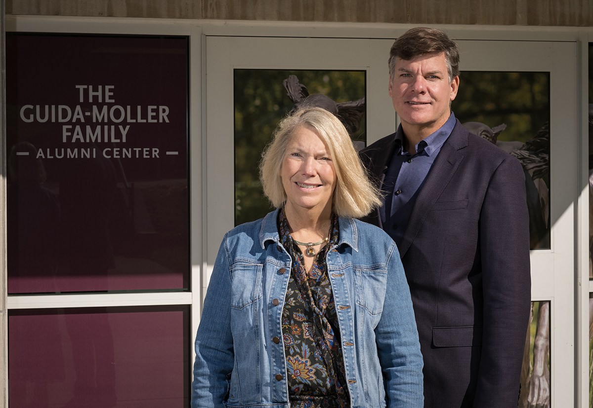 Image of Julie Guida and Scott Moller standing beside sign that reads Guida-Moller Family Alumni Center.